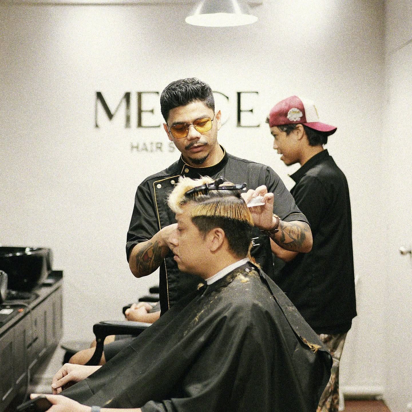 A barber cutting hair under the Merce Hair Studio wall sign